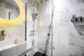 Bathroom tiled in white marble with gray veins, circular mirror and shower cabin with glass partition and square sink, soap and Royalty Free Stock Photo