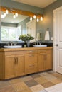 Bathroom vanity with wood cabinets, double sinks, slate tile floors and accent lighting in contemporary upscale home interior Royalty Free Stock Photo