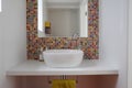 Bathroom wash basin with colorful glass mosaic tiles and mirror inset into the tiles