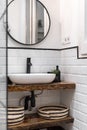 Bathroom with white brick walls, an oval washbasin on a wood-style marble top, a round mirror on a dark-framed wall