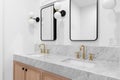 A bathroom with a white oak cabinet, marble countertop, and black and gold sconces.