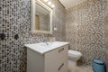 Bathroom with white wooden washbasin cabinet with drawers, mirror with white wooden frame and walls covered with mosaic tiles