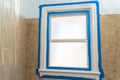 Bathroom window covered in blue painters tape inside of shower, ready for the trim to be painted white