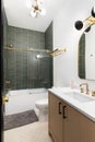 A bathroom with a wood cabinet, green tiled shower, and herringbone tile floor.