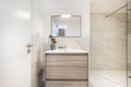 Bathroom with wooden cabinet of drawers with white porcelain sink, mirror with matching frame, marble tiles and shower cabin with Royalty Free Stock Photo