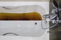 A bathtub filled with dirty water due to a clogged sewer pipe before and after cleaning the drain, close-up