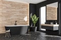 Bathtub and vanity in black bathroom with wood-look tiles. Corner view