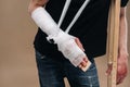 A battered man with a bandaged head and a cast on his arm stands on crutches on a gray background Royalty Free Stock Photo