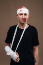 A battered man with a bandaged head and a cast on his arm stands on crutches on a gray background Royalty Free Stock Photo