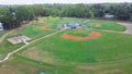 Batting cages with multiple baseball and softball fields, stadium seating in sport complex park surrounding by lush green tree in