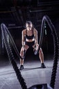 Battle ropes session. Attractive young fit and toned sportswoman working out in fitness training gym