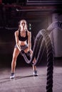 Battle ropes session. Attractive young fit and toned sportswoman working out in fitness training gym Royalty Free Stock Photo