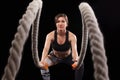 Battle ropes session. Attractive young fit and toned sportswoman working out in functional training gym doing exercise