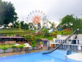 Batu, Indonesia - February 22, 2022: swimming pool, water slide, tent, Ferris wheel and garden with blue sky at Selecta