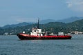 Red tug boat at sea with mountain background traveling in Black Sea Batumi harbor Georgia