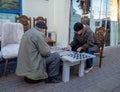 Men play backgammon in the street. People behind the intellectual game. Time spent in retirement