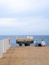 Two sit on the pier with their legs dangling. Two guys at sea. Friends met and talk on the old pier. Destroyed infrastructure at