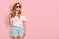 Bautiful girl in sunglasses, straw hat, summer blouse and short drinking summer cocktail, looking smiling aside, posing Royalty Free Stock Photo