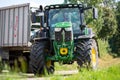 John Deere 6175R tractor drives with a Fliegl Gigant trailer on a dirt road