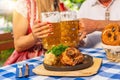 Bavarian couple clinking beer mugs with traditional Bavarian cuisine with Schweinshaxe, roasted ham hock in a beer garden or Royalty Free Stock Photo