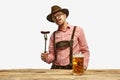 Bavarian mustache man in hat wearing traditional fest outfit holding hot fried sausage and looking at huge glass of beer Royalty Free Stock Photo