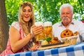 Bavarian women and old man clinking beer mugs with traditional Bavarian cuisine with roasted ham hock in a beer garden or Royalty Free Stock Photo