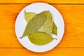 Bay leaf. Laurel tree leaves on a white plate on an orange wooden table. Culinary spices. Flavoring spices for cooking. Additives