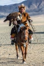 Kazakh Eagle Hunter at traditional clothing, on horseback while hunting to the hare holding a golden eagle on his arm