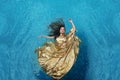 Bbeautiful young woman in gold dress, evening dress floating weightlessly elegant floating in the water in the pool Royalty Free Stock Photo