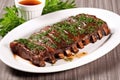 bbq beef ribs with tangy sauce and herbs on a white platter