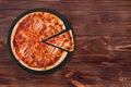 BBQ pizza with ham, bbq sauce, bacon and salami, with a slice slightly removed on slate black platter which is on wooden table Royalty Free Stock Photo