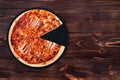 BBQ pizza with ham, bbq sauce, bacon and salami, without one slice on a slate black platter which is on wooden background Royalty Free Stock Photo