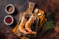 BBQ roasted Giant shrimps Langoustine on grill with herbs. Dark background. Top view