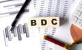 BDC text on wooden block on graph background with pen and magnifier