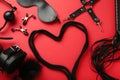 BDSM set on red background. BDSM accessories and rope in the shape of a heart. Mask, handcuffs, ball gag and a whip Royalty Free Stock Photo