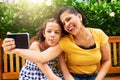 Be as goofy as you can. a young mother and her daughter taking selfies while sitting on a bench in the park. Royalty Free Stock Photo