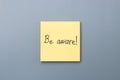 Be aware on yellow sticky note over a grey background. april fools day Royalty Free Stock Photo