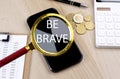 BE BRAVE text on the magnifier with smartphone, calculator and coins