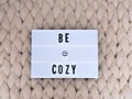 BE COZY word on lightbox on knit background. Cozy compozition. Knit background. Royalty Free Stock Photo
