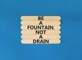 Be fountain not drain symbol. Concept words Be a fountain not a drain on wooden stick. Beautiful blue table blue background.