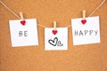 Be happy handwriting lettering on 3 white papers pinned with 2 big red heart pegs and one small red heart pegs on cork board