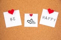 Be happy handwriting lettering on 3 white papers pinned with 2 big red heart pegs and one small red heart pegs on cork board