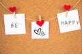 Be happy lettering with hearts on 3 white paper pinned with 2 small red heart pegs and one big red heart pegs on cork board