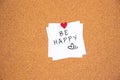 Be happy lettering on white paper pinned with red glowing heart-shaped thumbtack on cork board