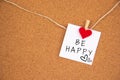 Be happy lettering on white paper pinned with small felt heart pegs on cork board