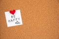 Be happy lettering on white paper pinned with thumbtack to the top left on cork board