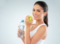 Be healthy, be happy. Studio shot of a fit young woman holding a bottle of water and an apple against a gray background. Royalty Free Stock Photo
