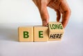 Be here belong symbol. Businessman hand turns a cube and changes words `be here` to `belong`. Beautiful white background. Busi