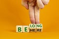 Be here belong symbol. Businessman hand turns cubes and changes words `be here` to `belong`. Beautiful orange background. Busi