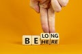 Be here belong symbol. Businessman hand turns cubes and changes words `be here` to `belong`. Beautiful orange background. Busi